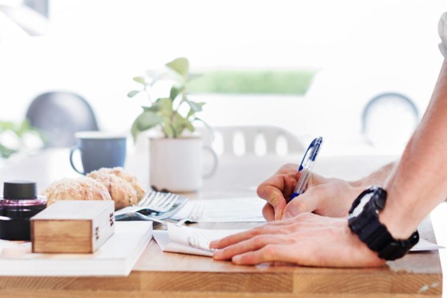 a hand wearing a black watch writing a letter