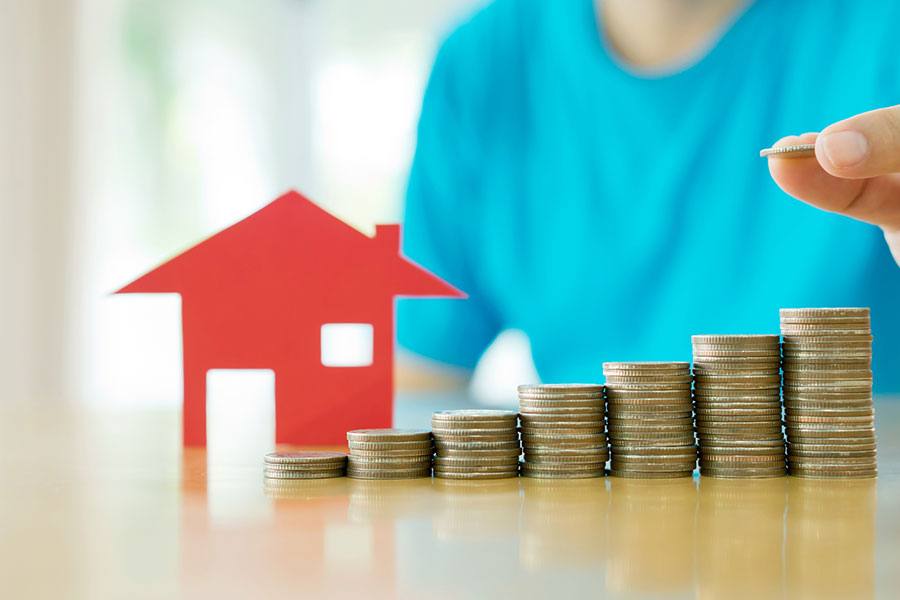 Miniature red house with stacks of coins