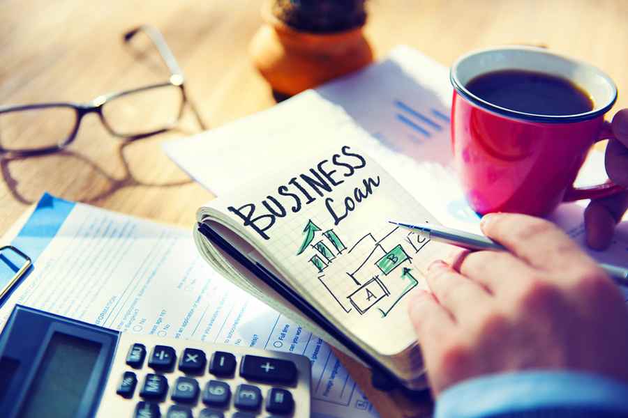 Business loans written in a notebook with coffee beside and a calculator.