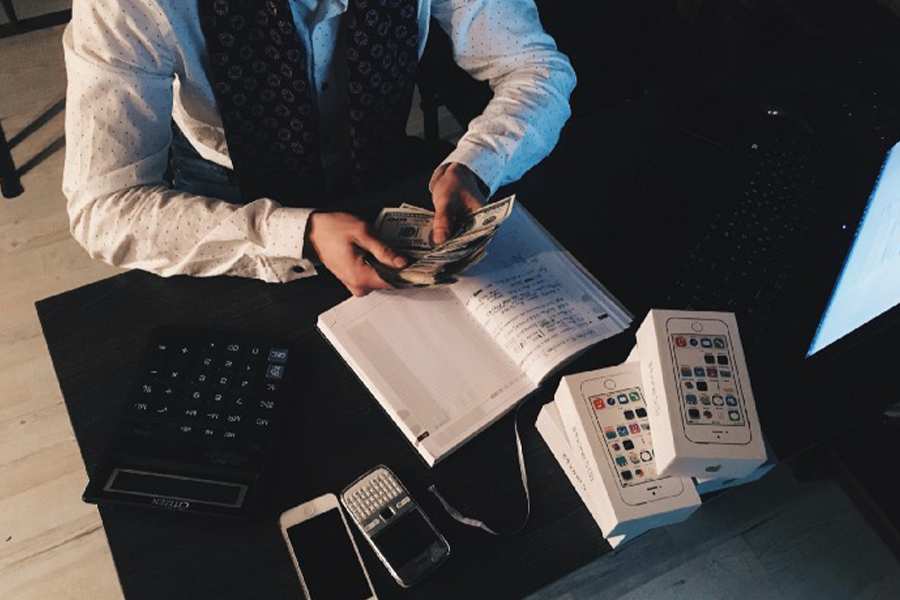 一名男子拿着现金数钱，面前放着计算器、笔记本、手机和盒子。