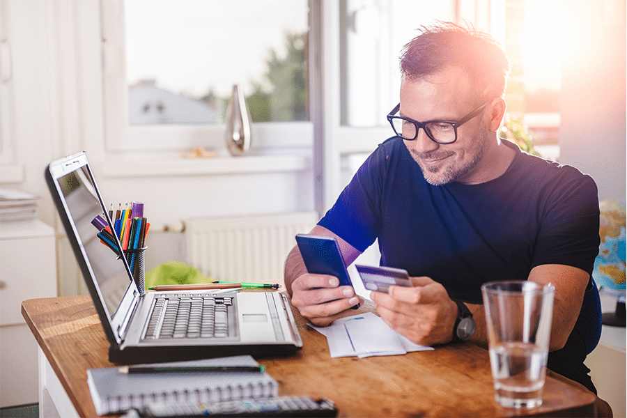 Man holding a phone and credit card in front of his laptop.