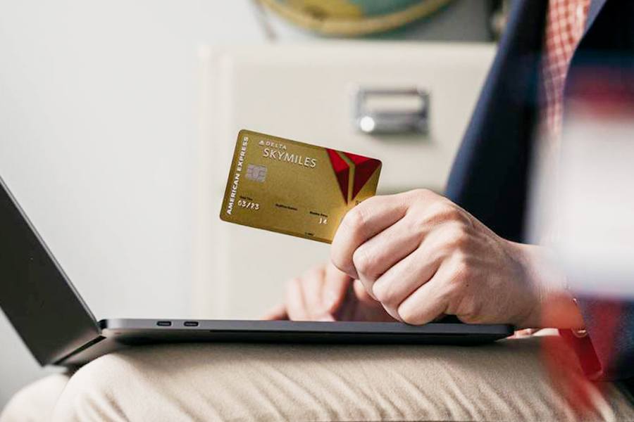 Man holding a Delta Skymiles credit card while working on his laptop.