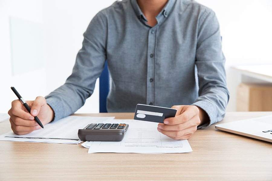 一名男子拿着信用卡和计算器在桌子上工作。