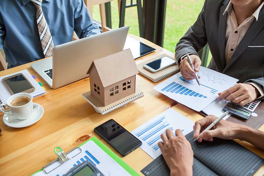 Professionals discussing reports with a wooden house on the table.