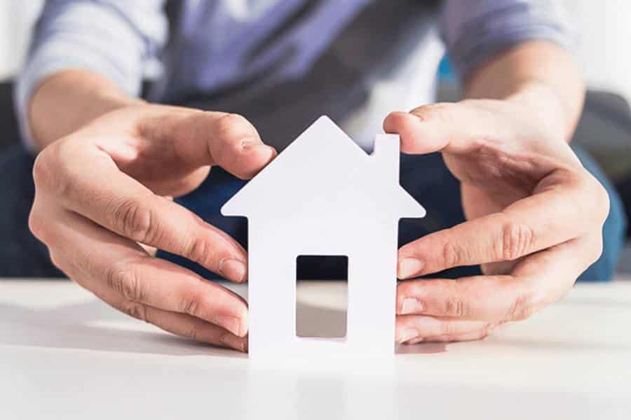 Businessman supporting the house model with his hands to stand.