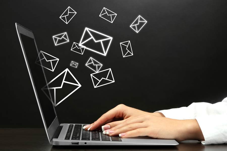 Woman hands typing on a laptop and some email icons flying out from the screen.