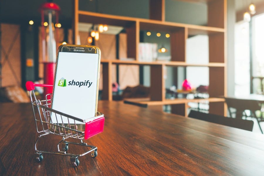 手机屏幕上的Shopify应用程序和木桌上的购物车。