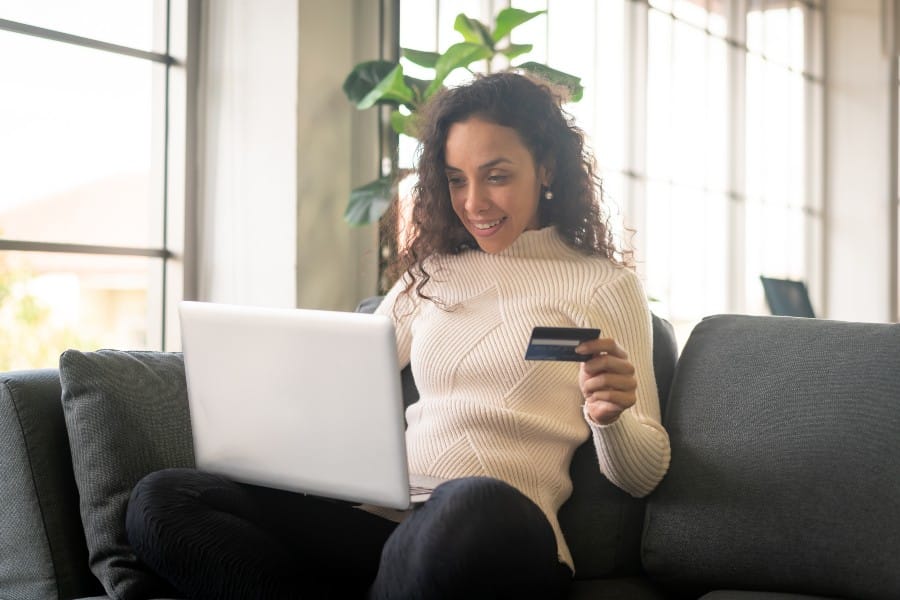 Woman using laptop while holding a credit card on her left hand.