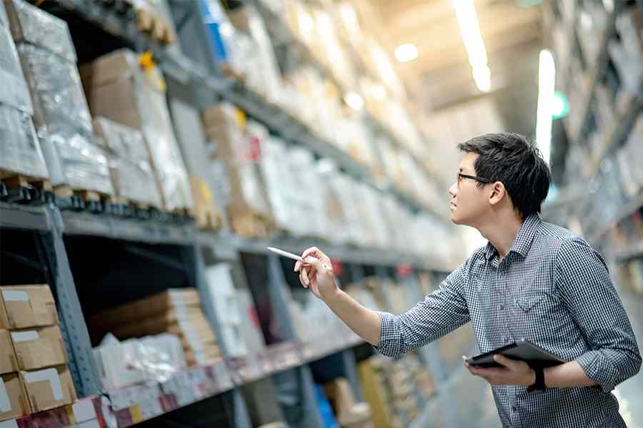 A man holding a tablet and a pen while doing an inventory of stocks.