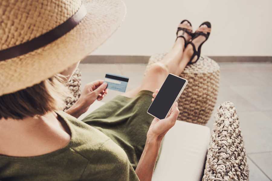 年轻女子在度假时一边用手机一边拿着信用卡。