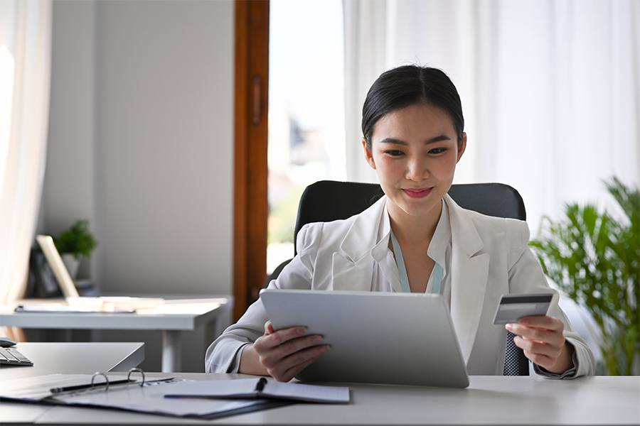 Young woman holding credit card and using tablet device.