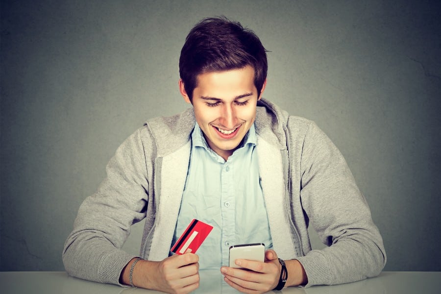 男子手持信用卡，用智能手机在网上购物。