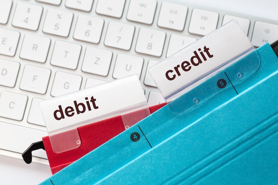 Two hanging folders in red and in blue on a keyboard having tabs with the words debit and credit on it.