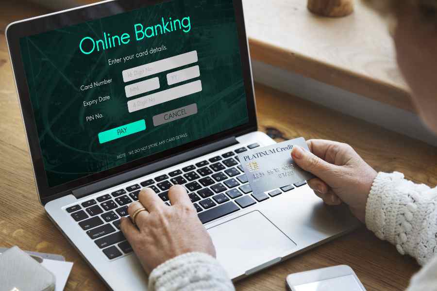 一名男子拿着信用卡在笔记本电脑上注册了一家网上银行。