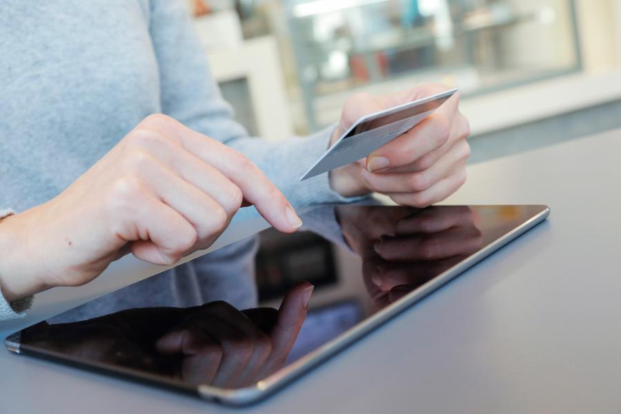 A woman holding a credit card and while using a tablet.