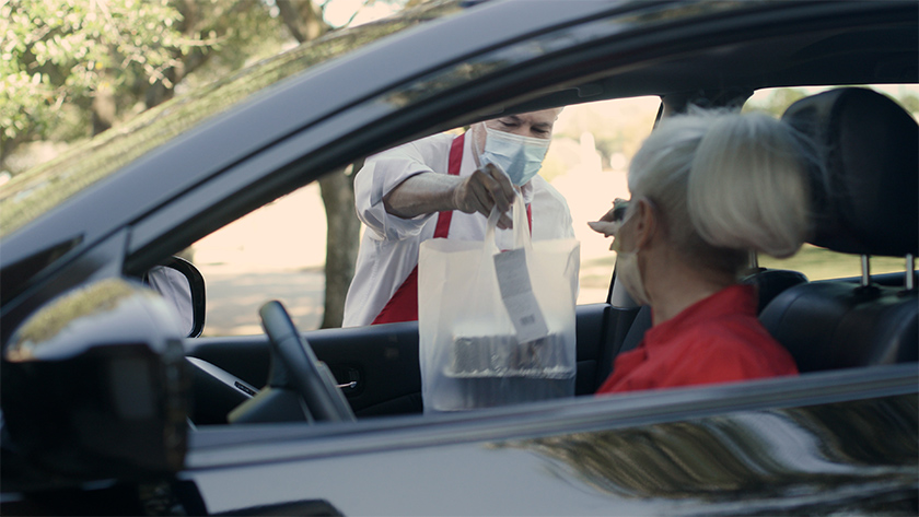 把焦点放在餐厅的工作人员，他把这位女士在路边点的食物从她的车的副驾驶窗口放出来。