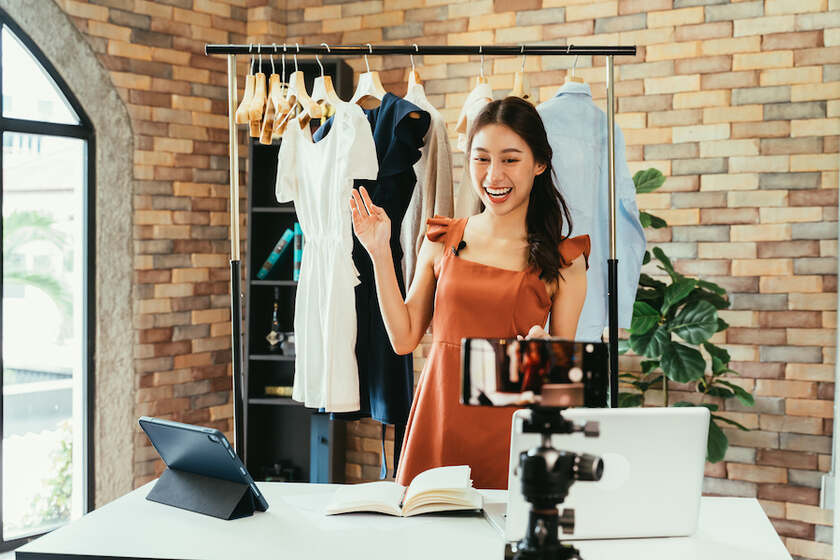 年轻女子在衣架前直播卖衣服。