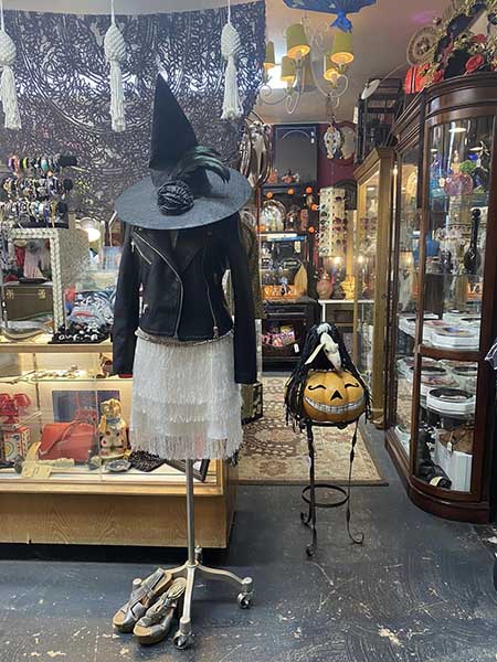 Dress form fitted with leather jacket, white skirt, and witch's hat displayed at an antique store.